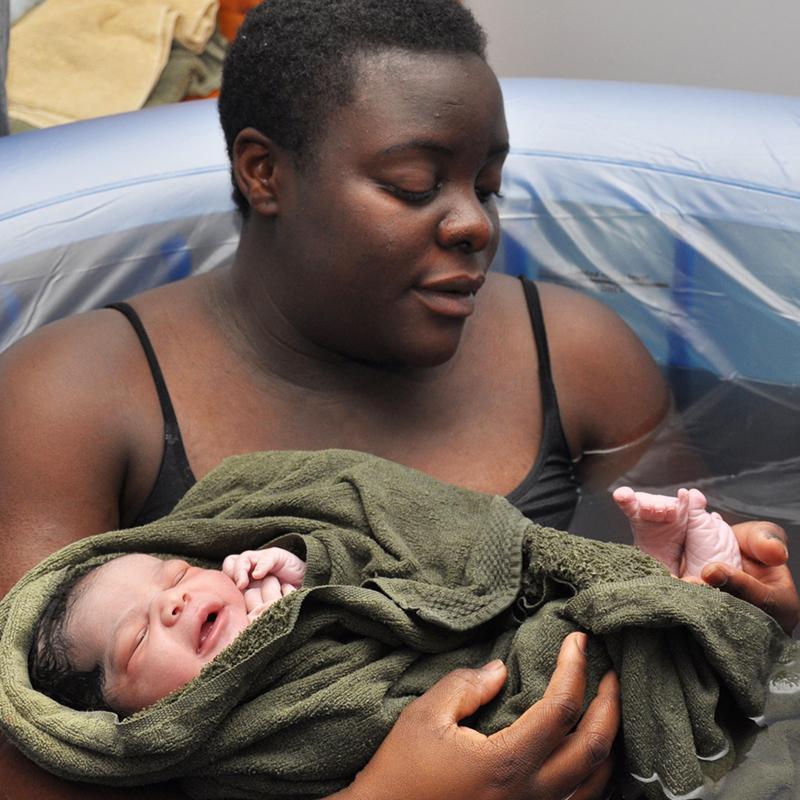 A Black woman craddling her infant just after giving birth in a water birth setting